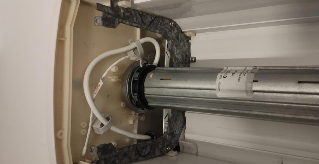 Moteur tubulaire blanc de porte de garage installé au plafond d'un garage résidentiel avec rail de guidage métallique et télécommande radio noire au premier plan sur établi